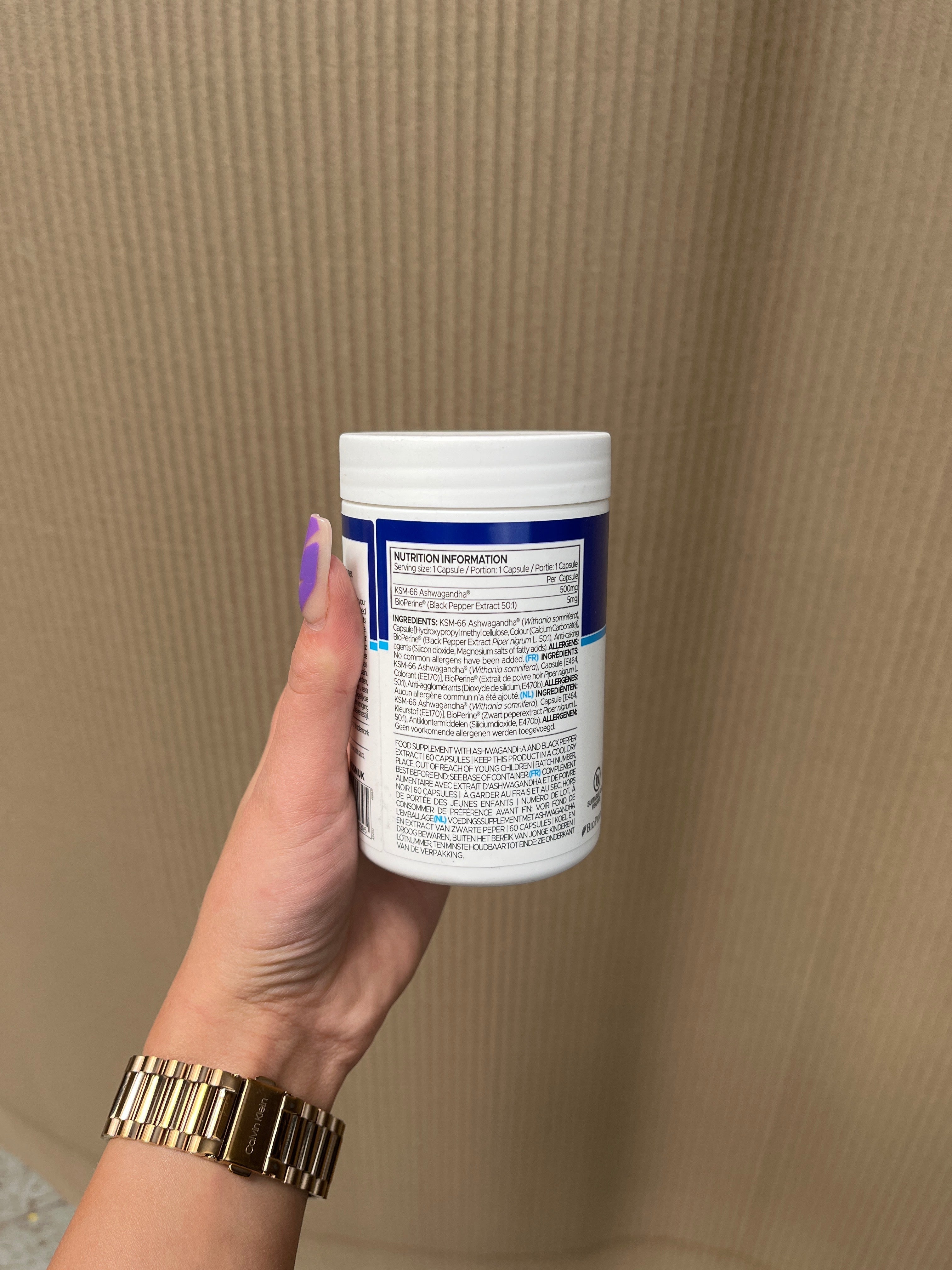 White USN Ashwagandha container with blue label, hand holding with purple nails
