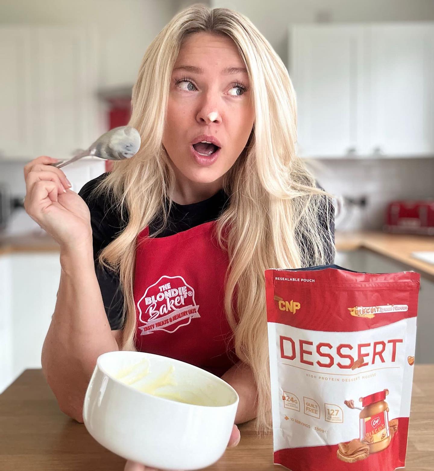 Woman with flour on nose holding spoon and bowl next to CNP Professional Dessert mix for a guilt-free treat