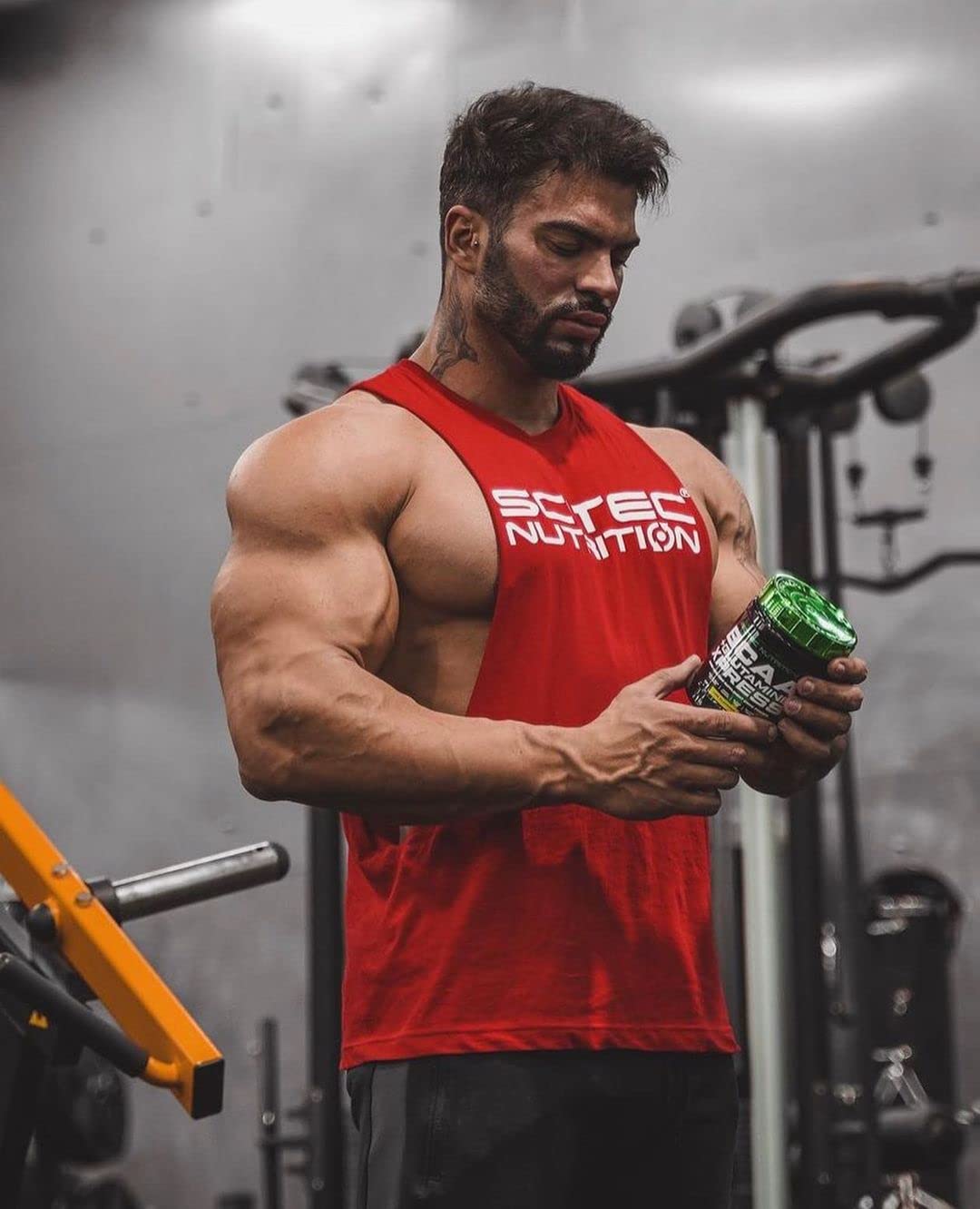 Muscular man in red tank top holding Scitec Nutrition BCAA Glutamine Xpress container
