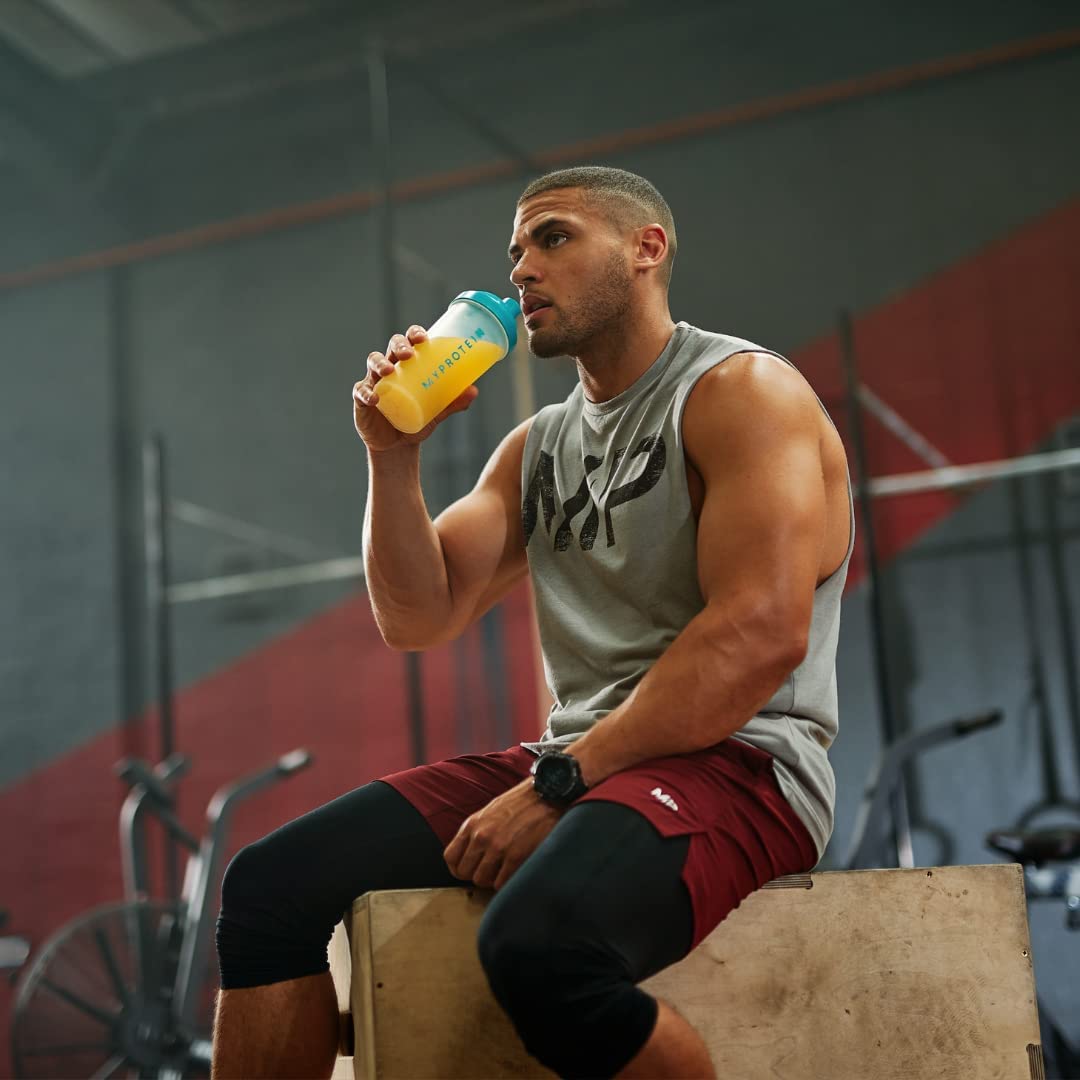 Fitness enthusiast in grey tank top and red shorts drinking clear whey isolate protein from shaker bottle