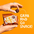 Hand holding a package of Keto Balls and a single protein ball snack from The Protein Ball Co