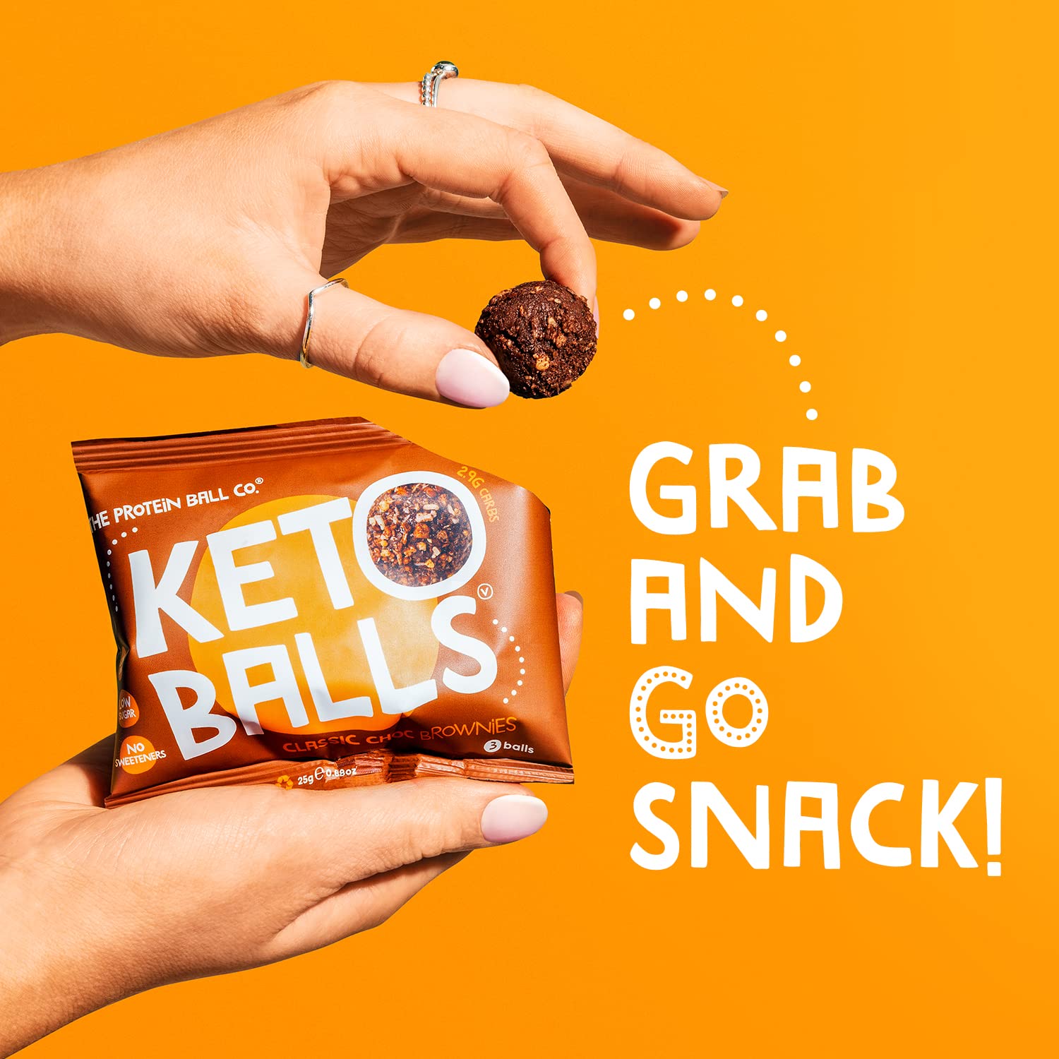 Hand holding a package of Keto Balls and a single protein ball snack from The Protein Ball Co