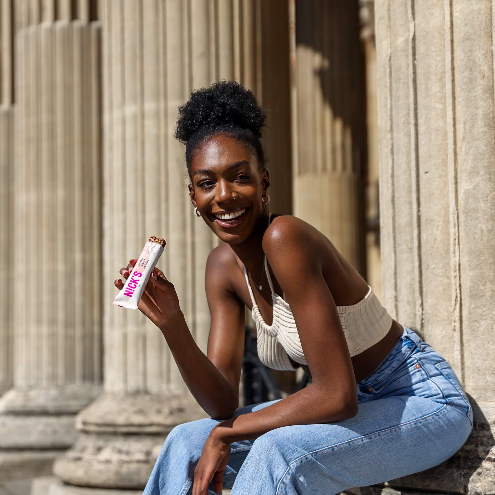 Smiling young woman with dark skin holding NICK’S Nut Bar made with vegan nut and cocoa butter