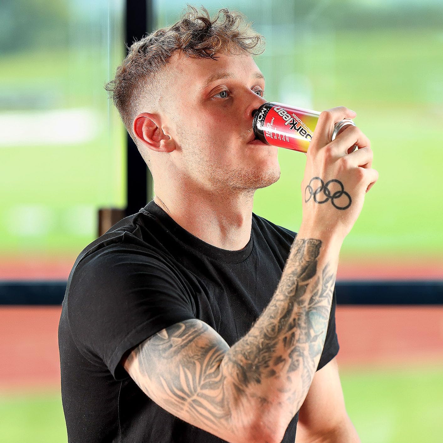 Man drinking VOW Nutrition Sparklean protein drink with colorful can and tattooed arms