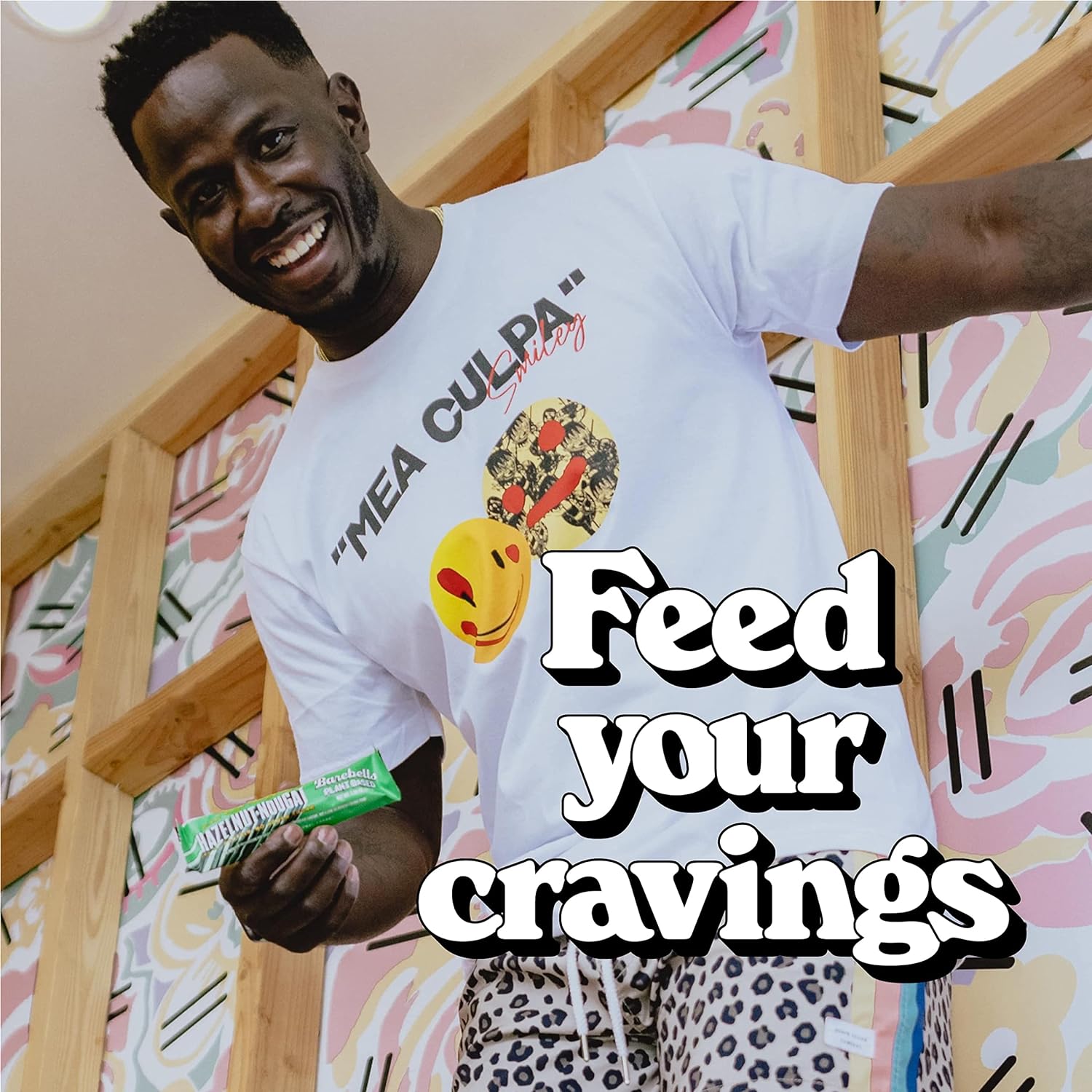 Man in white t-shirt and leopard shorts holding Barebells Vegan Protein Bar