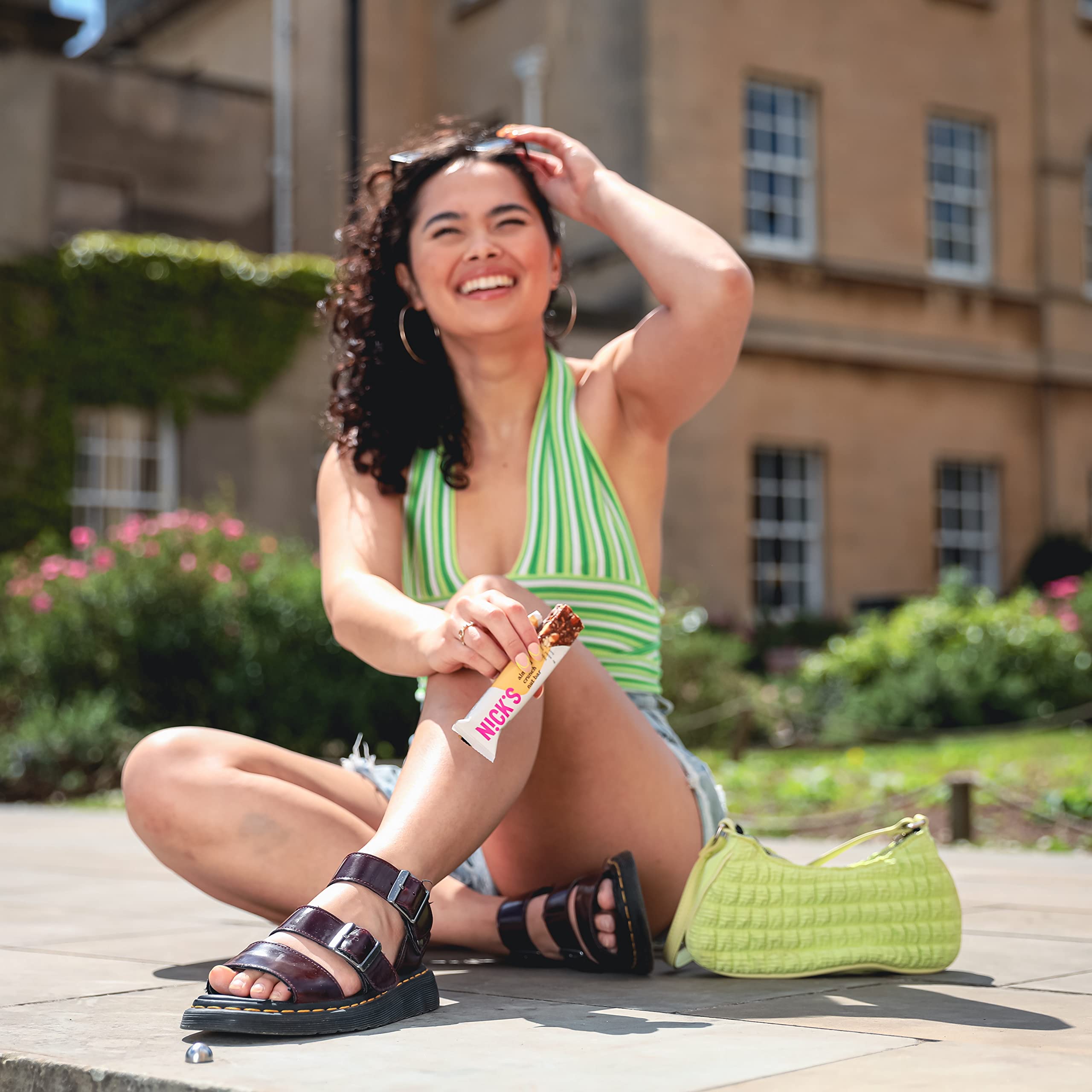 Smiling woman with dark curls in striped top holding NICK’S Nut Bar with vegan nut and cocoa butter