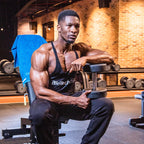Muscular man in black tank top holding dumbbell with BioTech USA Vitamin C 1000 supplement