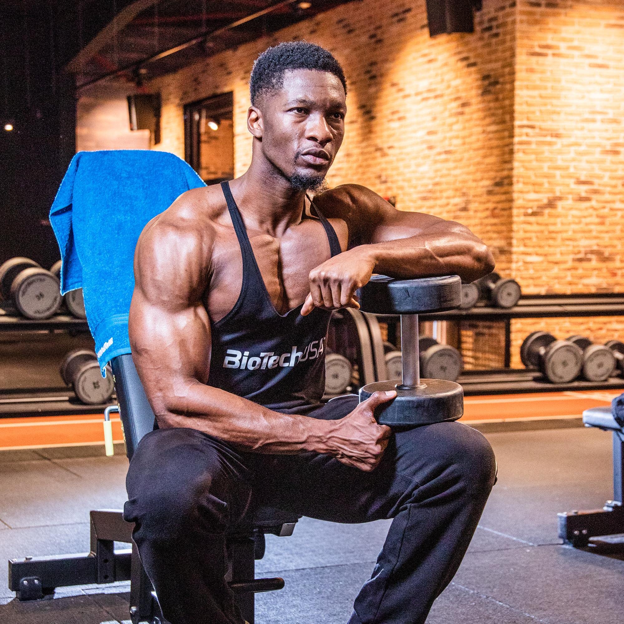 Muscular man in black tank top holding dumbbell with BioTech USA Vitamin C 1000 supplement