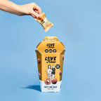 Dropping a gold-wrapped chocolate into LoveRaw Nutty Choc Balls container for vegan indulgence