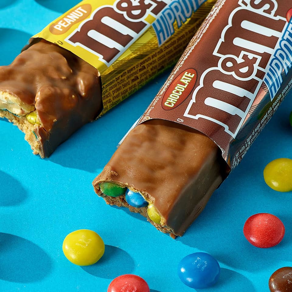 M&M Hi-Protein Bar with peanut and chocolate, colorful M&Ms around it