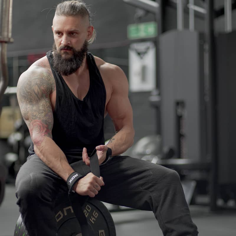 Muscular man with beard lifting RDX Training Weight wrist straps with wicking properties
